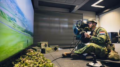 Een viertal afbeeldingen. Naast het cilindervormige, donkergroene antitankwapen Spike Long Range gericht op een beamer, hetzelfde middel alleen nu met daarachter een militair. Samen met een instructeur, die achter een beeldscherm zit, bevinden de twee zich in een kleinere ruimte. Vervolgens diezelfde oefenende militair schuin vanaf onder en gezien vanaf voren. Daarbij is zijn geconcentreerde blik zichtbaar.