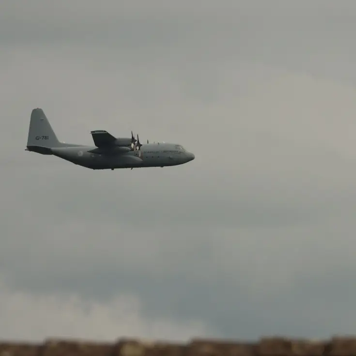  Een grijs militair vliegtuig vliegt onder een blauwe hemel over een dak van een huis.
