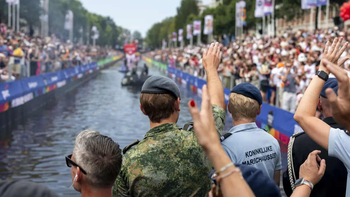 In de voorgrond wuiven militairen vanaf een bootje naar de menigte op de kanten naast de gracht.