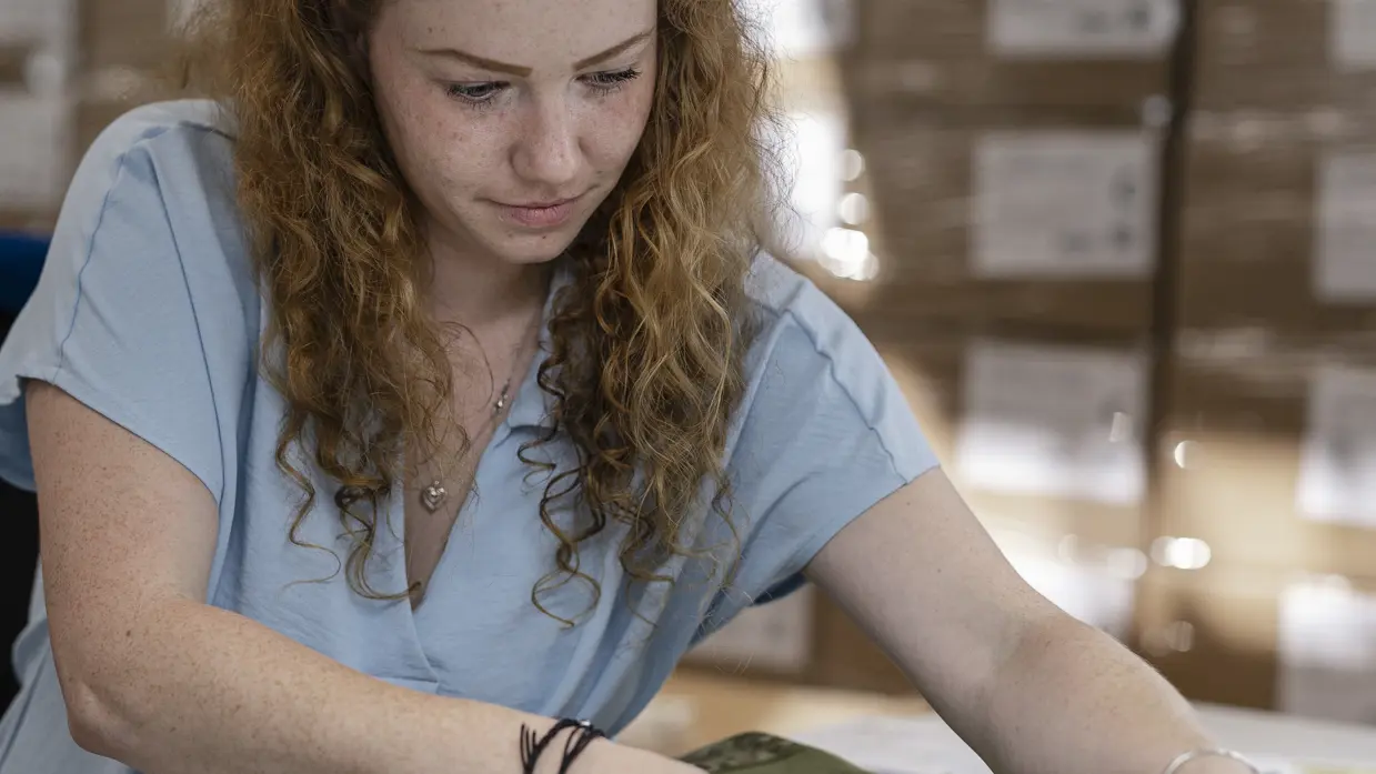 Een vrouw houdt een meetlint op een militair kledingstuk. 