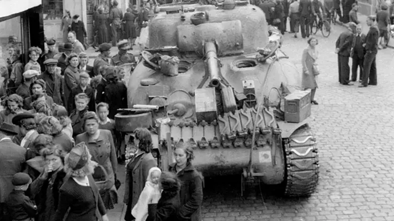 Een tank rijdt door een drukke straat, omringd door nieuwsgierige burgers in een zwart-wit stadstaferelen.    