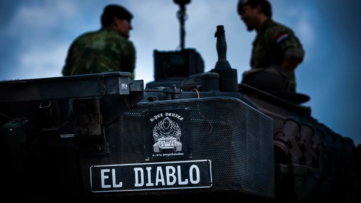 Een naamplaat met El Diablo op de achterkant van een tank, met het silhouet van twee militairen op de achtergrond.