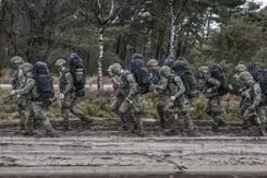 Militairen lopen over een modderig pad.