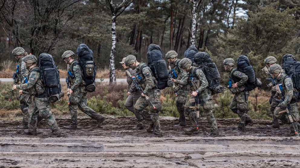 Militairen lopen over een modderig pad.