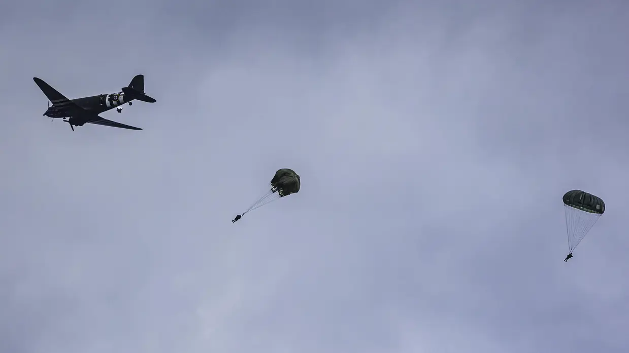  parachutisten springen uit een oud tweemotorig vliegtuig.