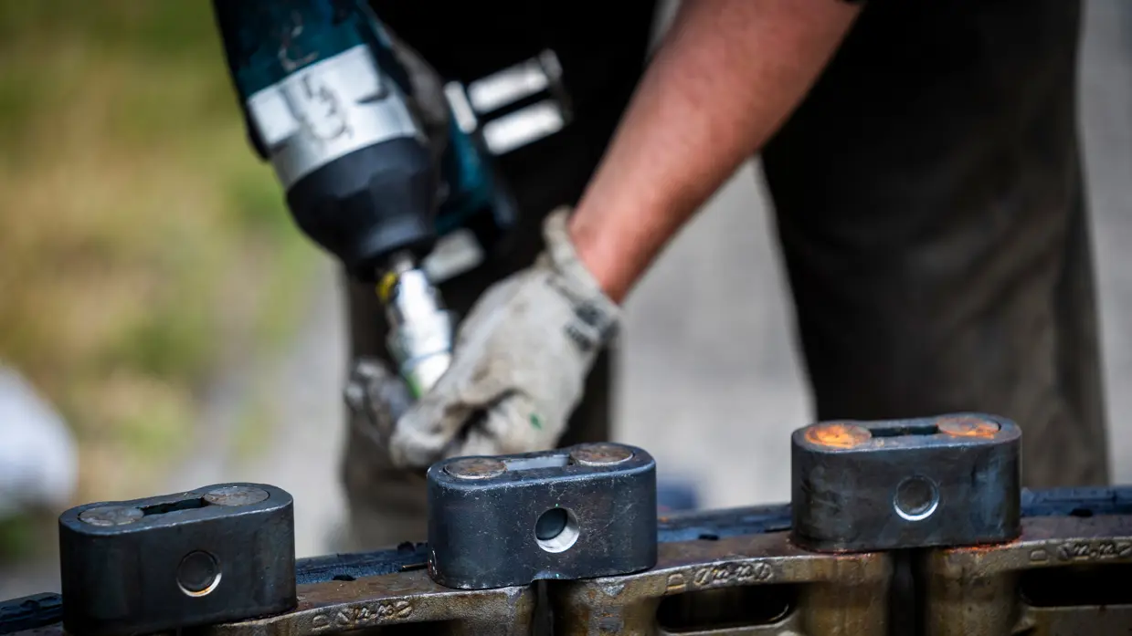 Handen in beschermende handschoenen gebruiken een boor om iets los te koppelen van een metalen constructie.