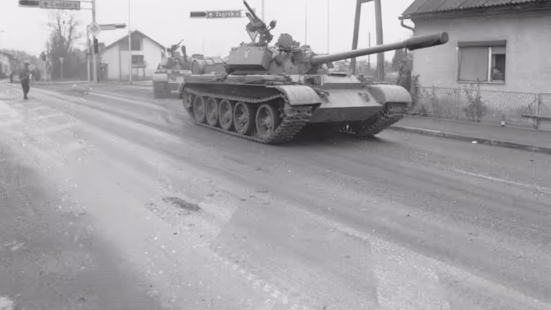 een tank rijdt langs een huis, met op de achtergrond een verkeersbord met daarop Zagreb.