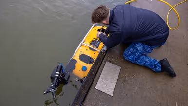 Een marinecollega zit gebogen op de kade en is bezig met een geel vaartuigje dat half onder water ligt. Op de andere foto bedient een marinecollega joysticks en kijkt naar een beeldscherm waarop onderwaterbeelden te zien zijn. 