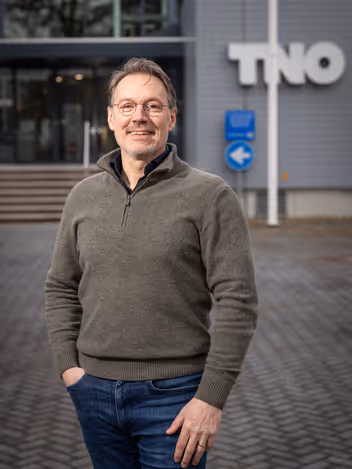 Portretfoto van Rajko Brokken. Vaag op de achtergrond is de afkorting TNO te zien.