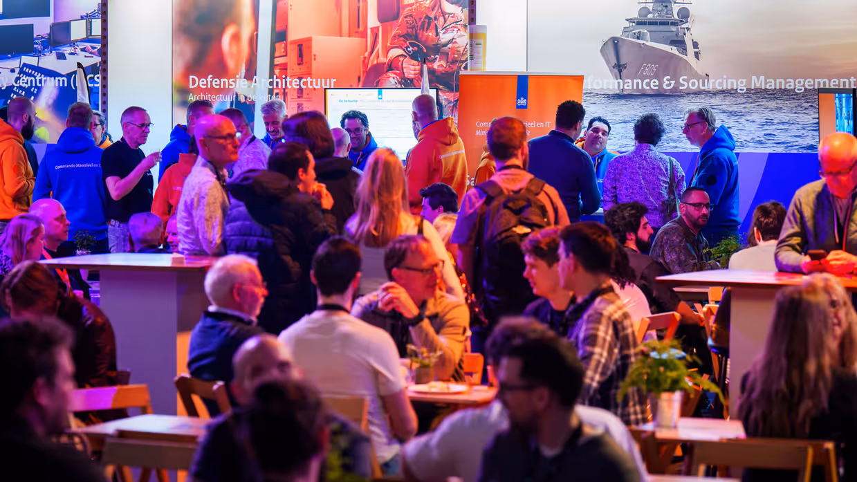 Conferentievloer gevuld met zittende en staande mensen in gesprek met elkaar.