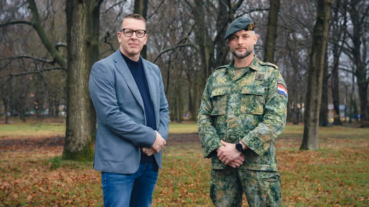Portretfoto van projectleider Michel en majoor Jean. De twee staan naast elkaar en hebben hun handen voor zich. Daarachter een bosrijke omgeving.