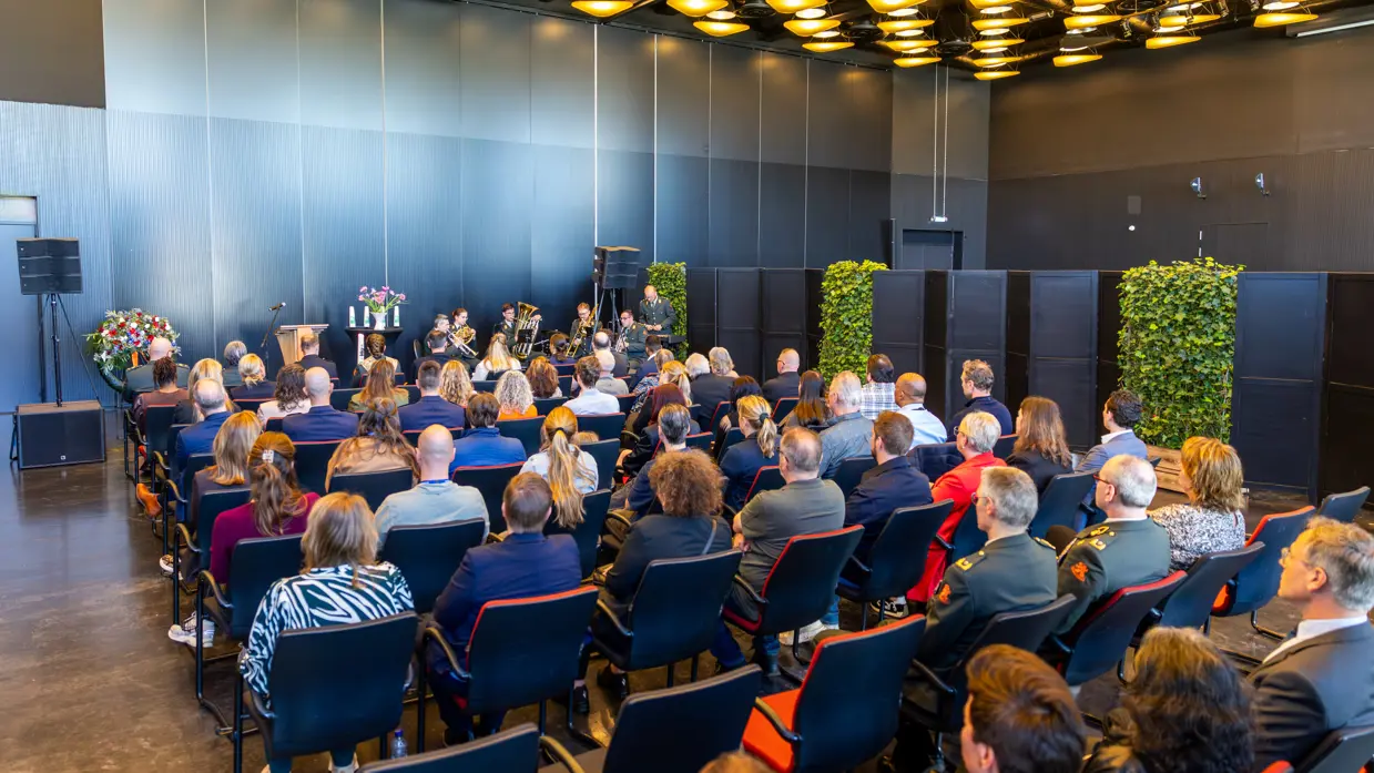 Een zaal gevuld met mensen, die kijken naar een zestal militairen in uniform dat muziek speelt.