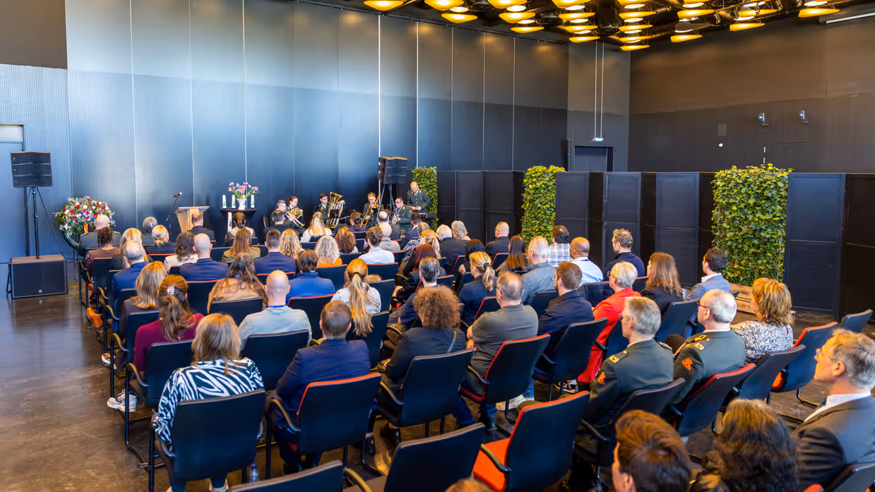 Een zaal gevuld met mensen, die kijken naar een zestal militairen in uniform dat muziek speelt.