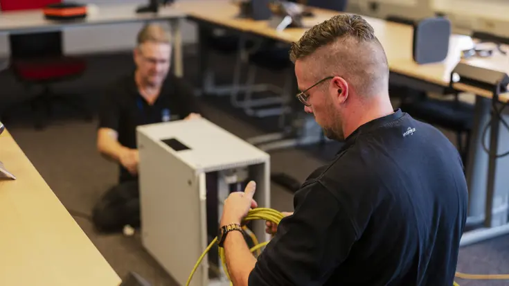 Twee ICT-medewerkers leggen netwerkkabels aan tijdens de opbouw van werkplekken voor Falcon Leap.