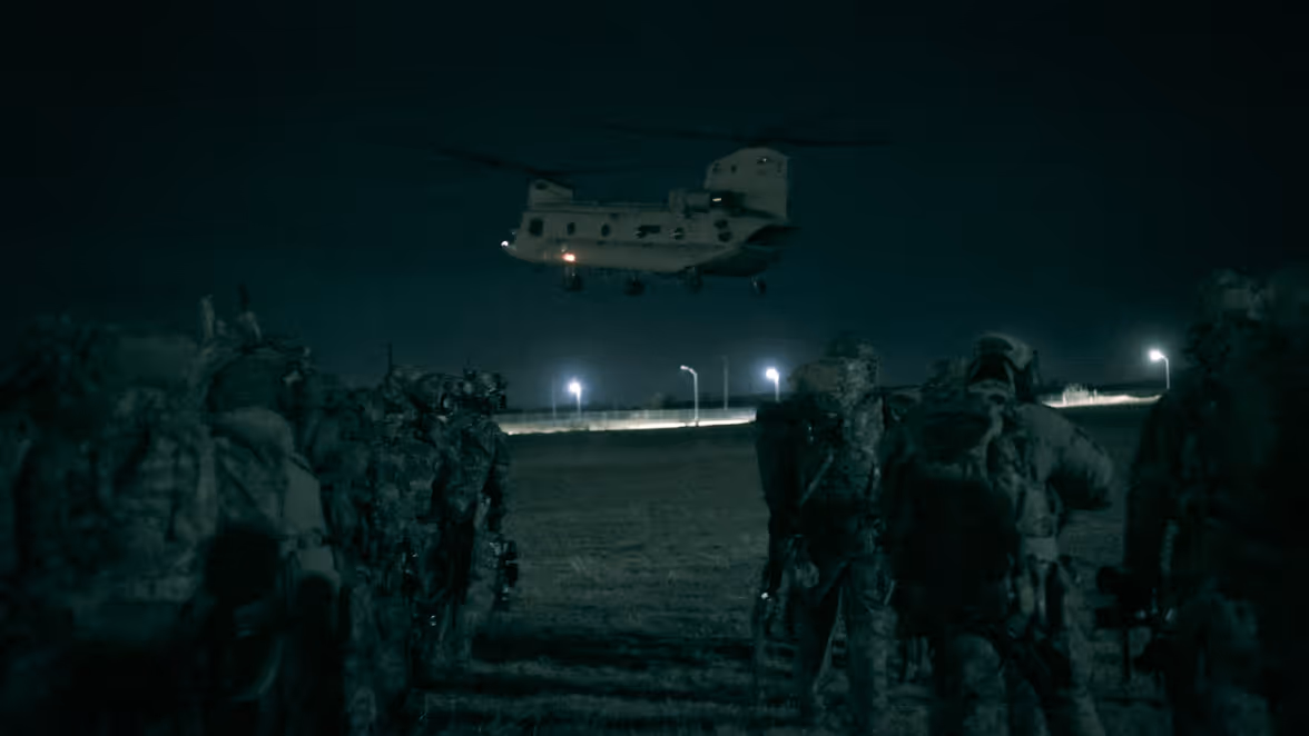 Alt-tekst: Chinook stijgt in duisternis op, op de voorgrond landmachtmilitairen. 