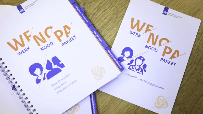 Witte boekjes liggen schuin naast elkaar op een tafel. Daarop de tekst ‘WENOPA’.