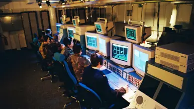 Een militair van de marine naast luchtmachters achter computerschermen. 