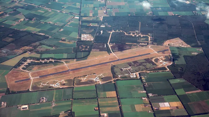 Luchtfoto van de voormalige Vliegbasis De Peel. Op het terrein zijn de startbaan, gebouwen en opstelplaatsen van de Patriot-squadrons zichtbaar.