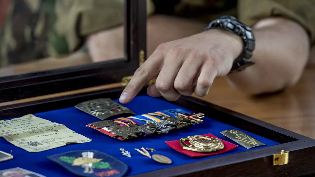 Een hand wijst naar militaire onderscheidingen in een koffer.