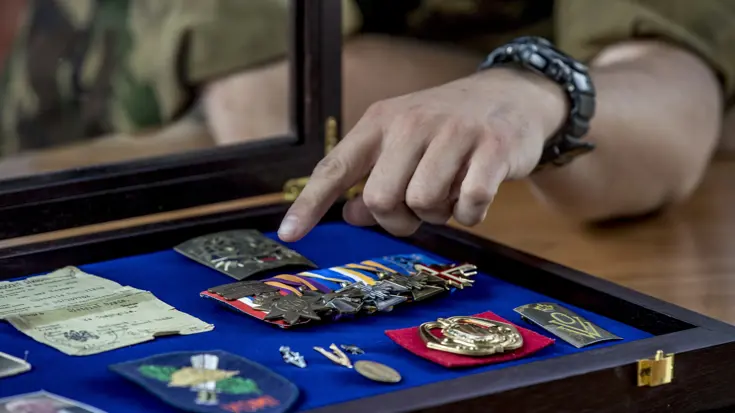 Een hand wijst naar militaire onderscheidingen in een koffer.