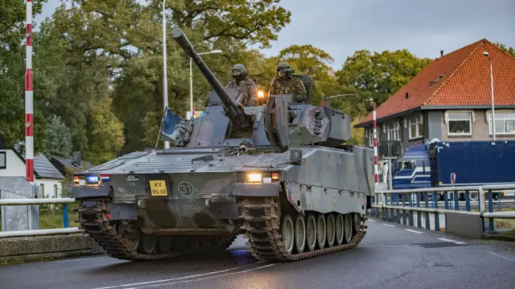 Tank rijdt over een brug, met aan weerskanten huizen.