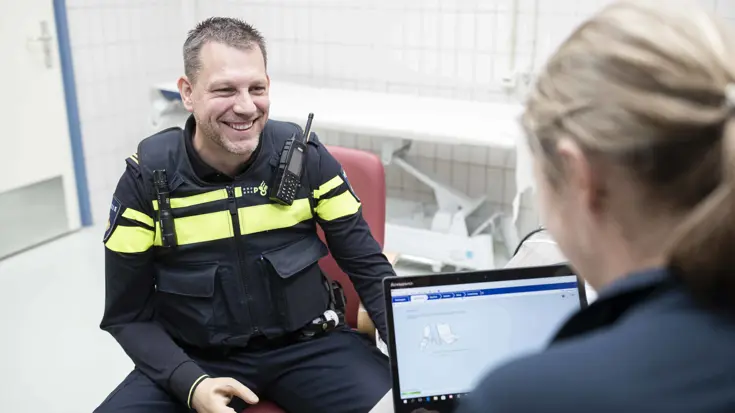 Politieagent met een handprothese zit tegenover een arts met een laptop.