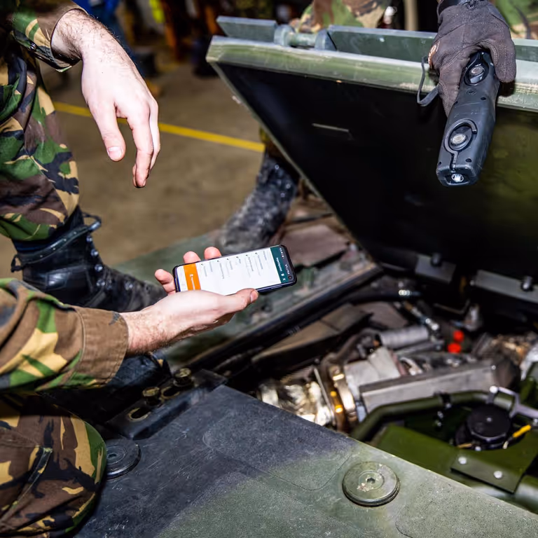Monteur met telefoon in hand tijdens onderhoud voertuig.