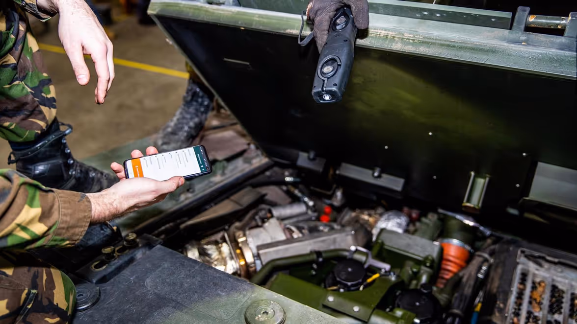 Monteur met telefoon in hand tijdens onderhoud voertuig.