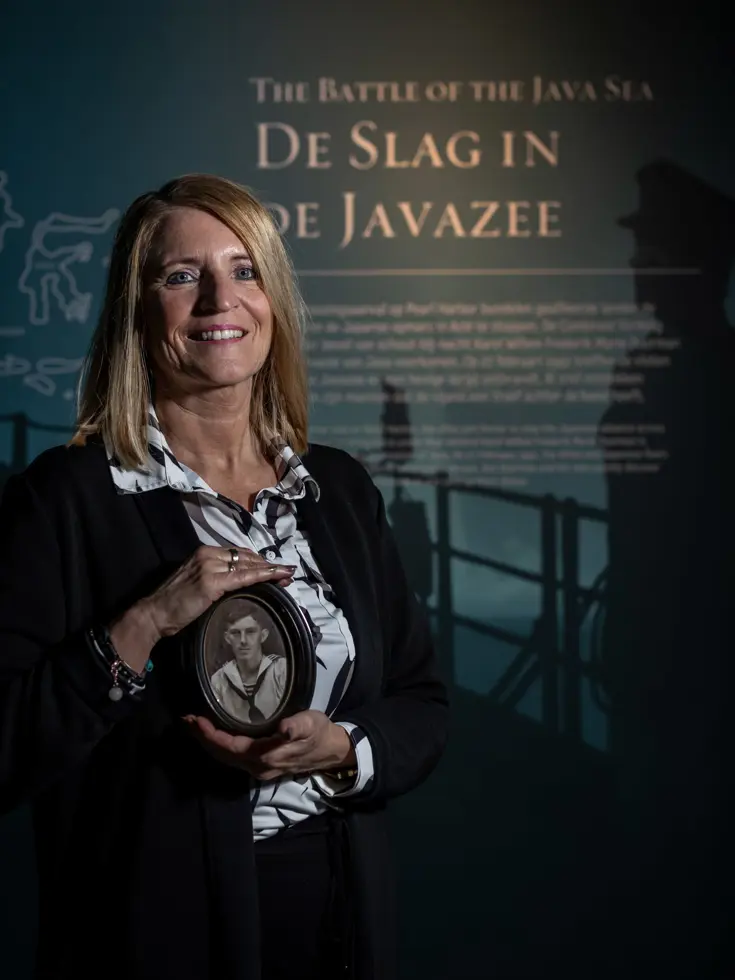 Vrouw met historische foto in de hand voor informatiebord 'Slag in de Javazee' bij Marinemuseum.