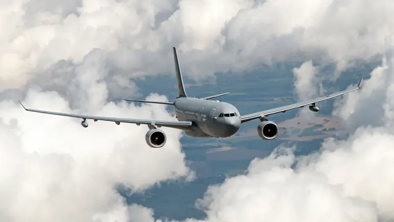 Vooraanzicht van een A330 MRTT, vliegend tussen de wolken met hier en daar stukken land zichtbaar.