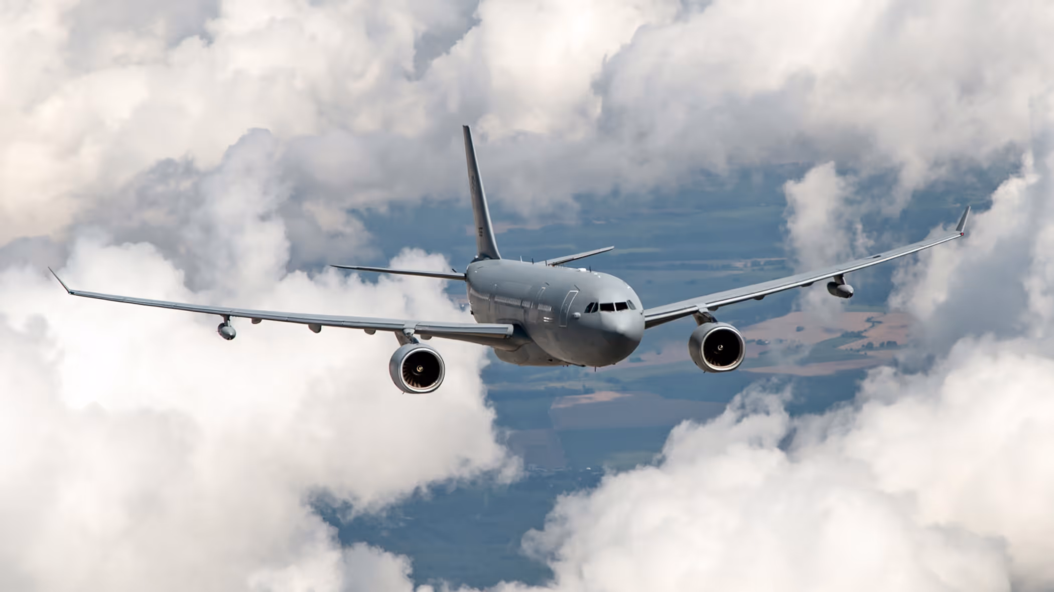 Vooraanzicht van een A330 MRTT, vliegend tussen de wolken met hier en daar stukken land zichtbaar.