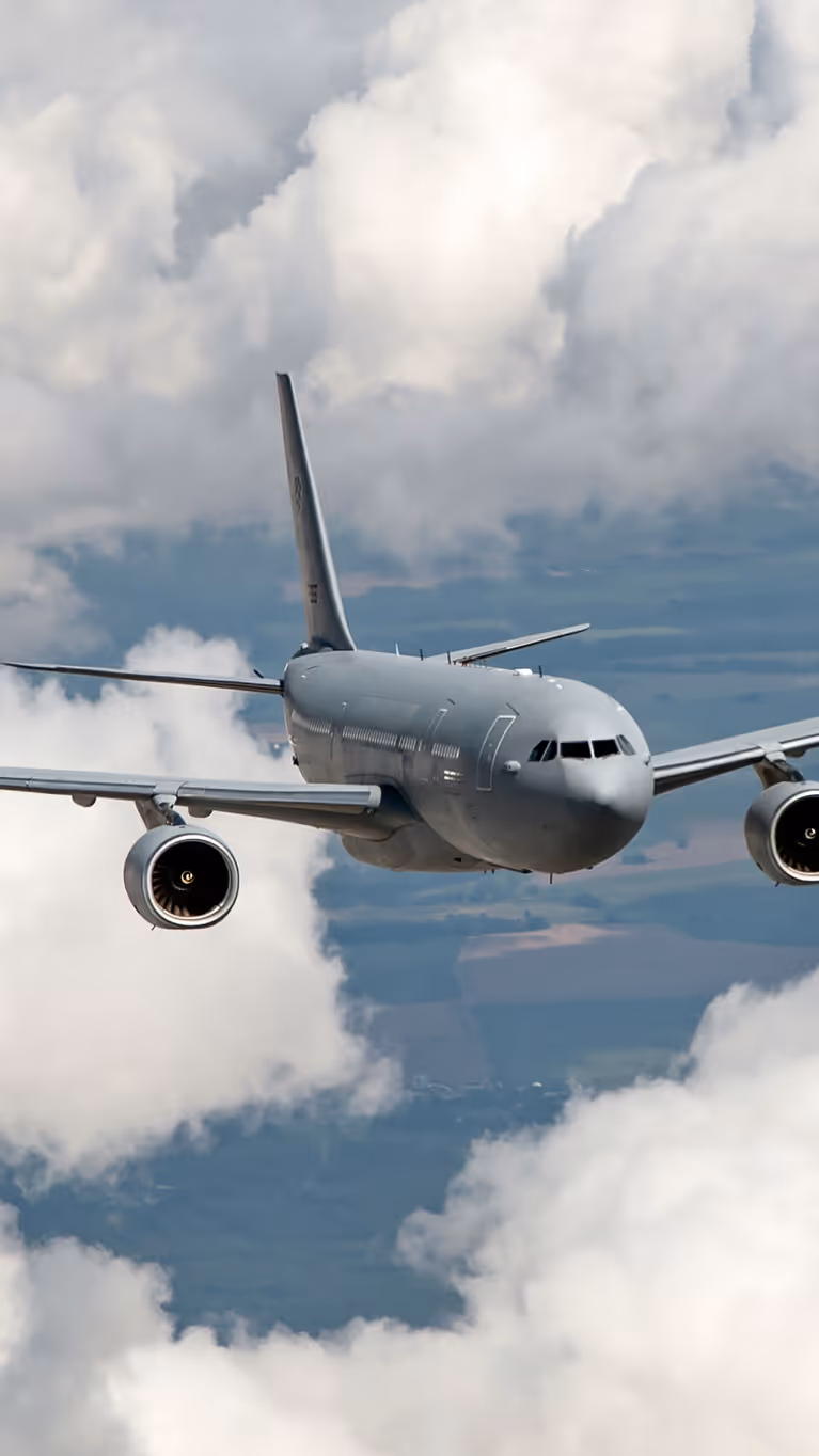 Vooraanzicht van een A330 MRTT, vliegend tussen de wolken met hier en daar stukken land zichtbaar.