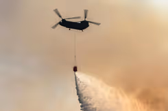 Chinook-transporthelikopter in oranjegekleurde lucht stort water uit met bambi-bucket onder het toestel.