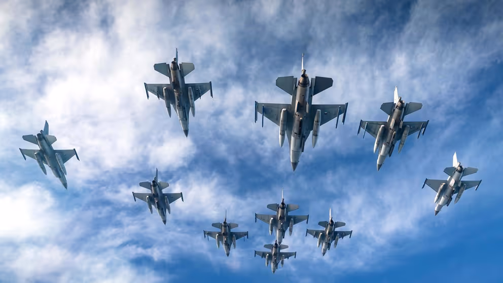 Vliegende F-16's met blauwe lucht en wolken op de achtergrond.