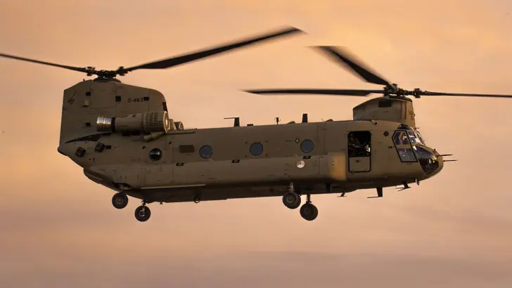 Een Chinook-transporthelikopter in een oranje gekleurde lucht.