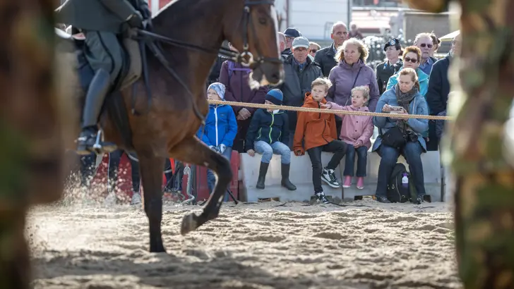 Publiek kijkt hoe militairen te paard oefenen voor Prinsjesdag op het strand.