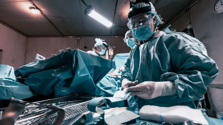 Een arts in groene operatiekleding knipt een verband.