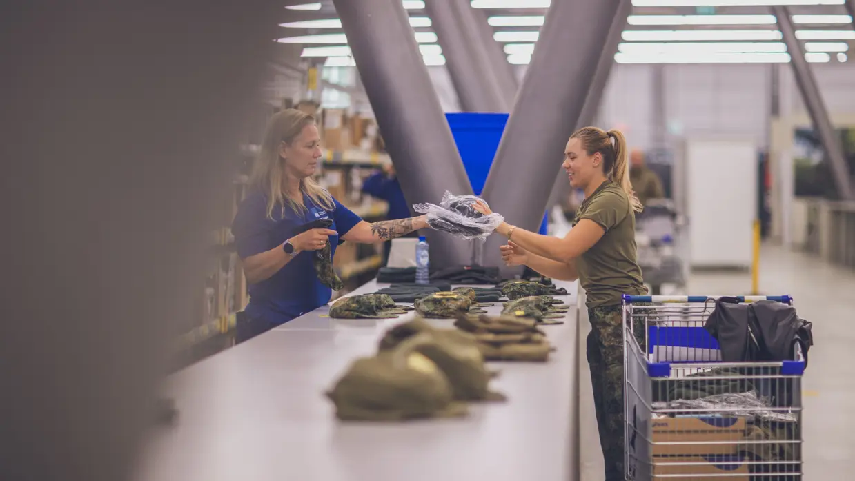 Militair krijgt kleding uitgereikt. In de winkelwagen achter haar liggen al meerdere stukken.