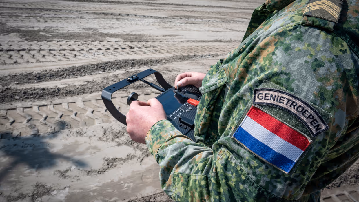 Een militair bedient een console voor een drone. Van de militair is enkel de romp te zien. Op zijn arm prijkt een eenheidsembleem van de genietroepen, plus een Nederlandse vlag.&nbsp;