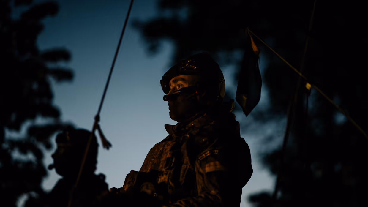 Het is donker. Er is een silhouet te zien van een militair die bovenluiks zit.