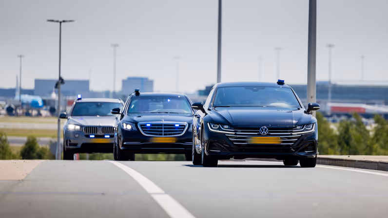 Drie geblindeerde auto’s rijden achter elkaar en hebben hun zwaailichten aan.