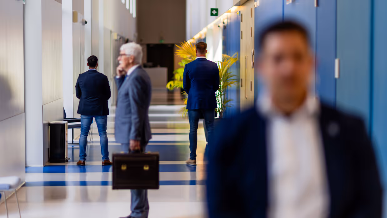 Drie persoonsbeveiligers staan in een gang en omringen een bellende man in pak. Daarnaast vier persoonsbeveiligers die rondom een man lopen bij het Binnenhof in Den Haag.