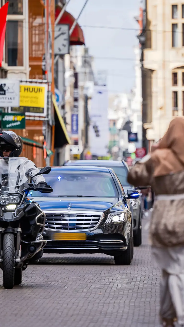 Twee auto’s met geblindeerde ramen rijden achter elkaar door een winkelstraat in Den Haag.