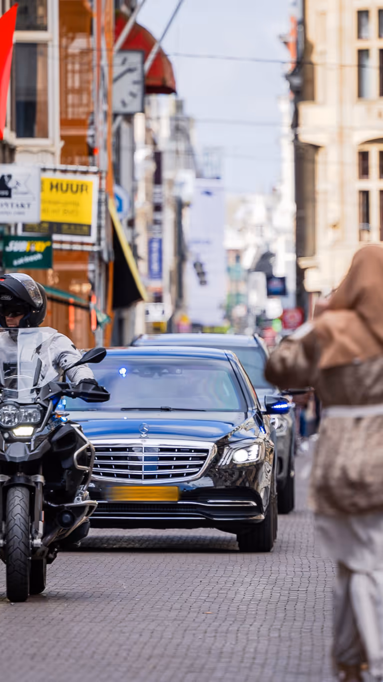 Twee auto’s met geblindeerde ramen rijden achter elkaar door een winkelstraat in Den Haag.