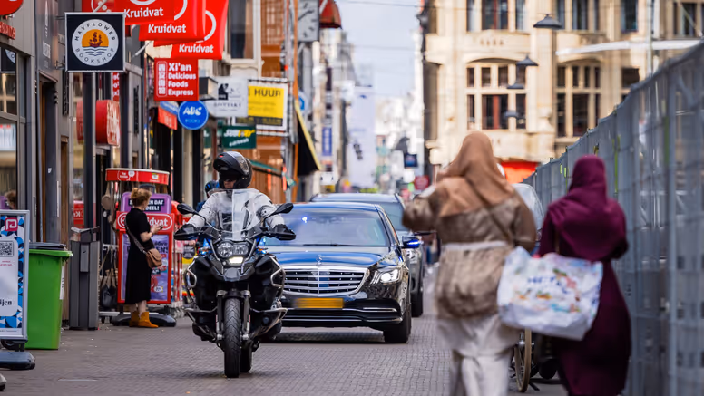 Twee auto’s met geblindeerde ramen rijden achter elkaar door een winkelstraat in Den Haag.
