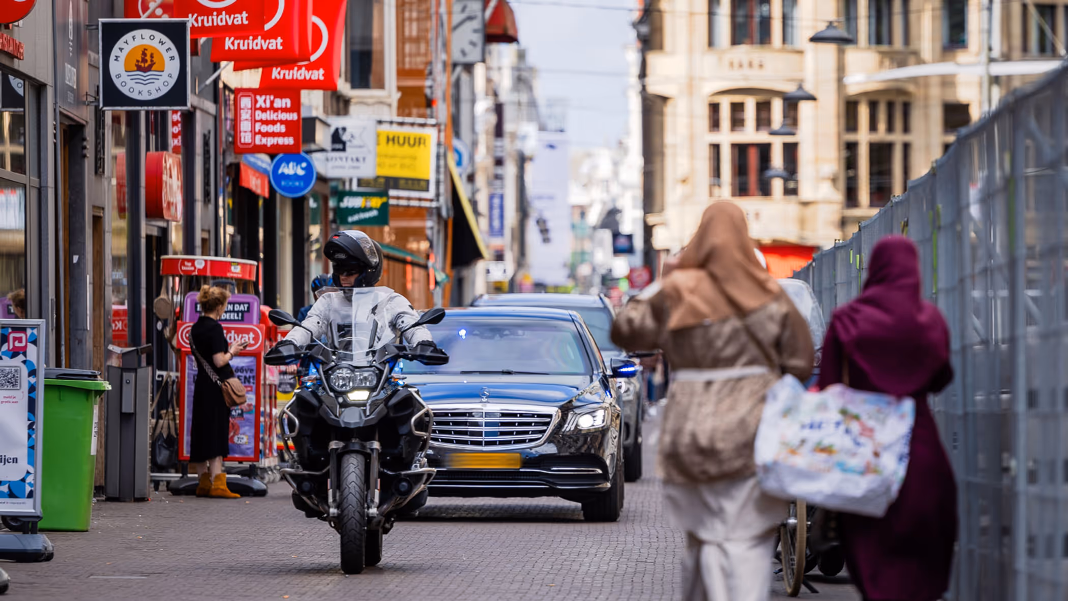 Twee auto’s met geblindeerde ramen rijden achter elkaar door een winkelstraat in Den Haag.