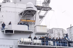 Militairen staan zwaaiend naast elkaar langs de reling van een marineschip.