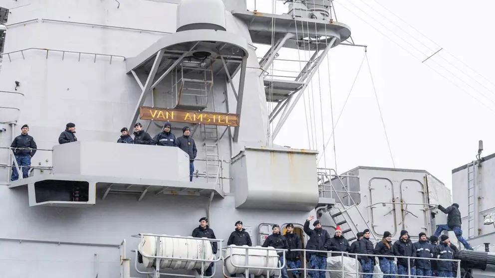 Militairen staan zwaaiend naast elkaar langs de reling van een marineschip.