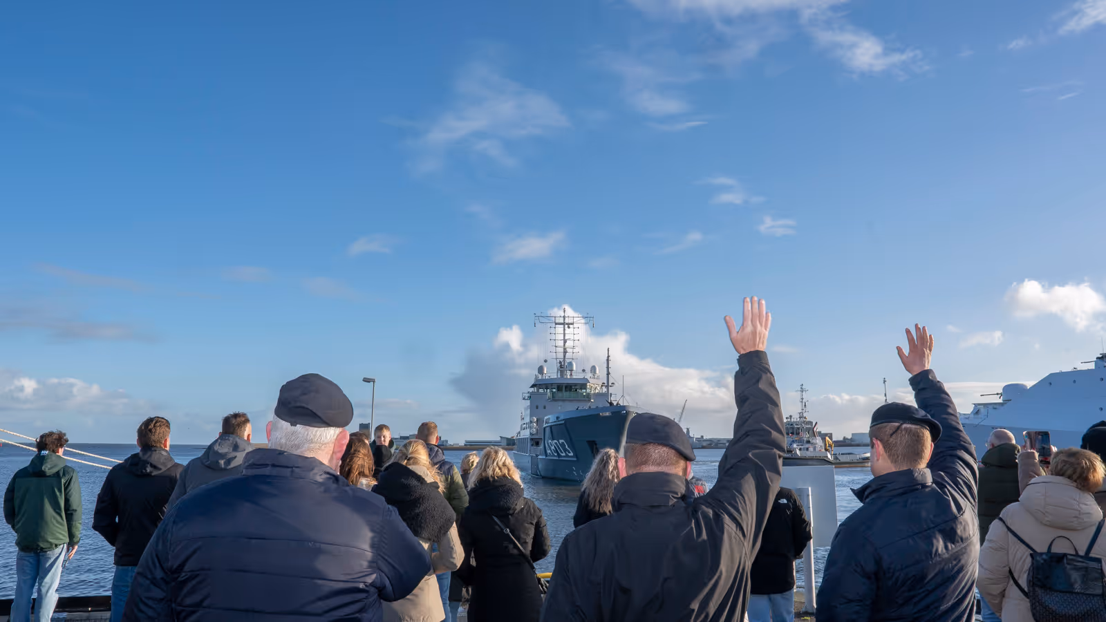 Mensen zwaaien een marineschip uit.