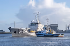 Een varende Zr.Ms. Luymes met een sleepboot erbij.